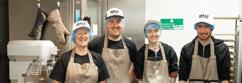 The team from Half the Story wearing aprons and white baseball hats standing over some biscuit dough